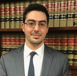 A man in suit and tie standing next to a book shelf.