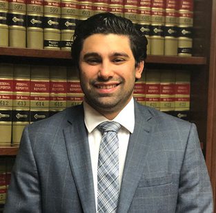 A man in suit and tie standing next to some books.