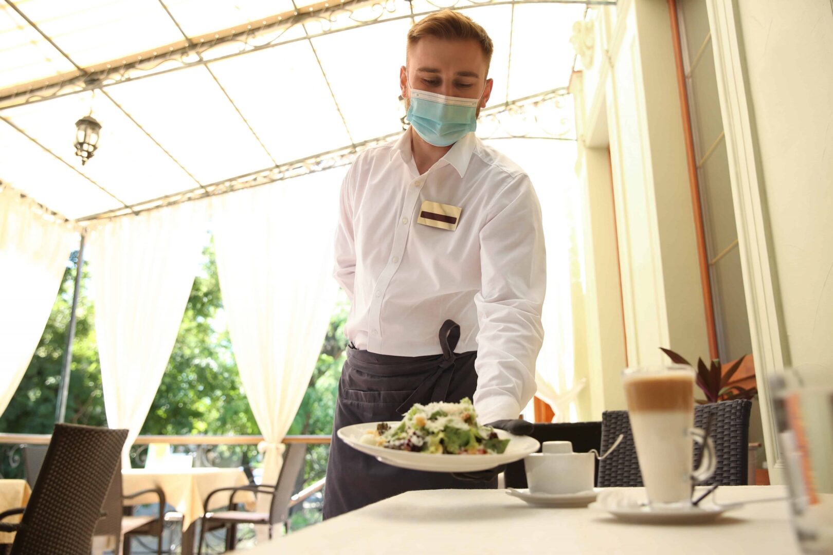 A waiter wearing a mask serving food to someone.